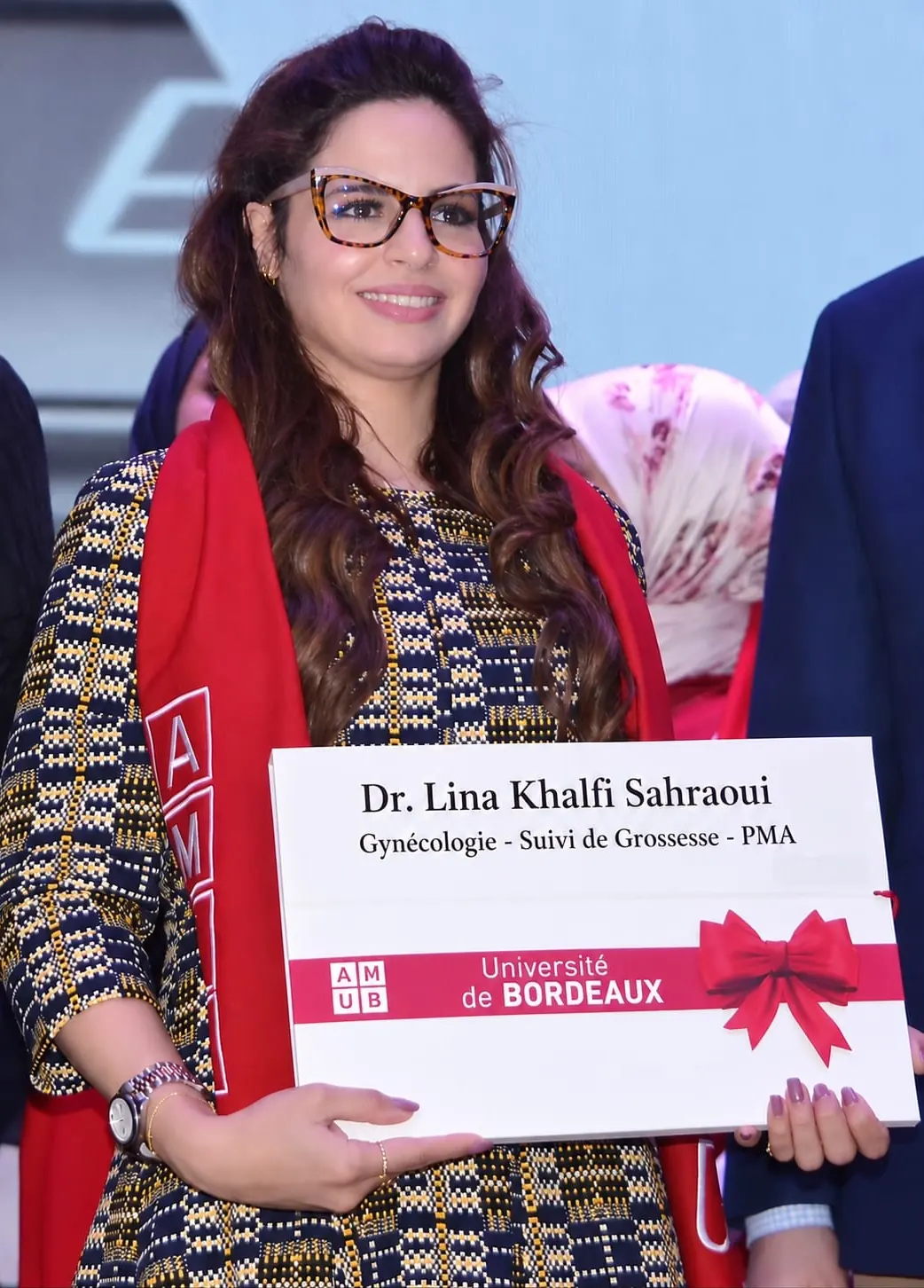 Dr Lina Khalfi Sahraoui lors d’une cérémonie, tenant un support aux couleurs de l’Université de Bordeaux